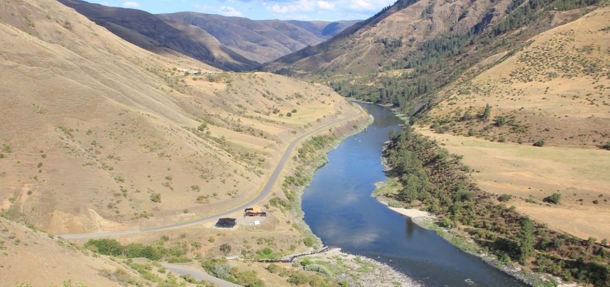 Image shows the blue Salmon River snaking through a sagebrush-covered gorge, viewed from up on the hillside. This is where Cooper's Ferry is located in Idaho.