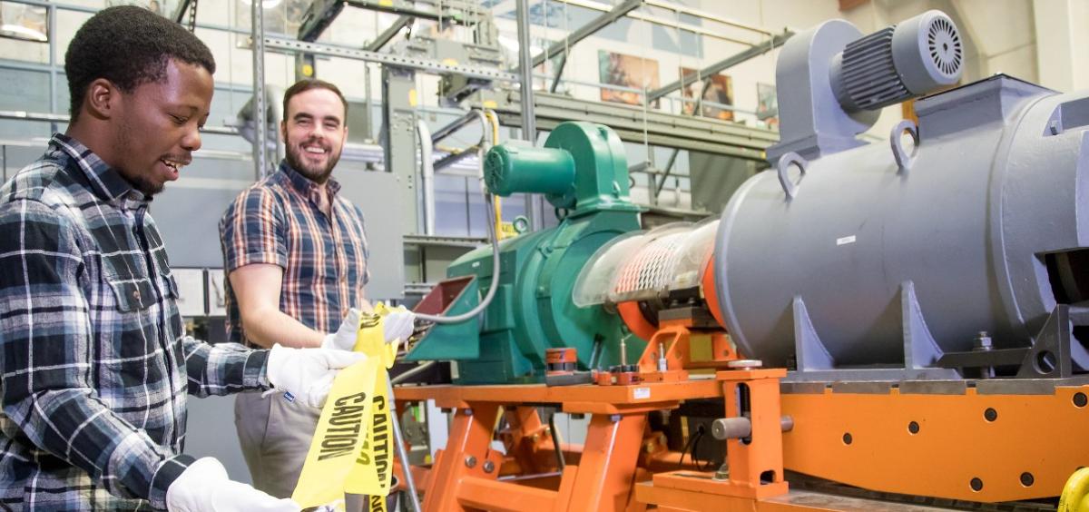 Ph.D. student Thabiso Mabote, left, and College of Engineering faculty member Eduardo Cotilla-Sanchez put caution tape around a machine testbed.