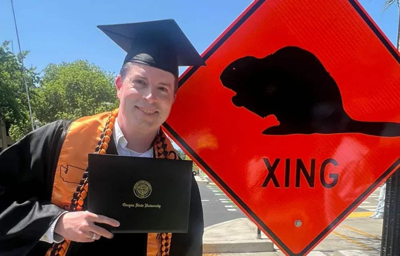 Graduate in front of beaver crossing sign