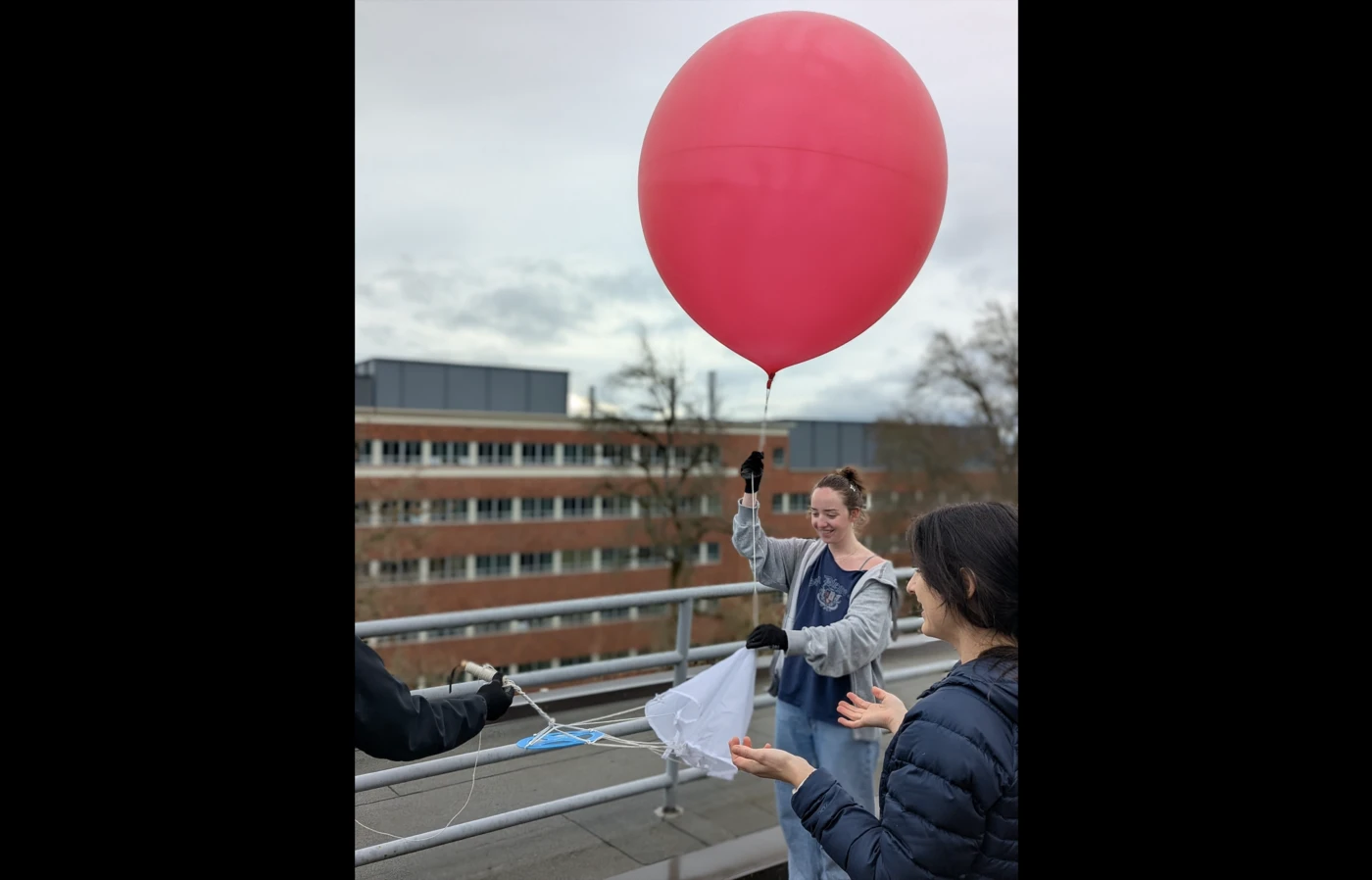 A student holds onto the tail of a big red weather balloon on the roof of an OSU building pre-launch.