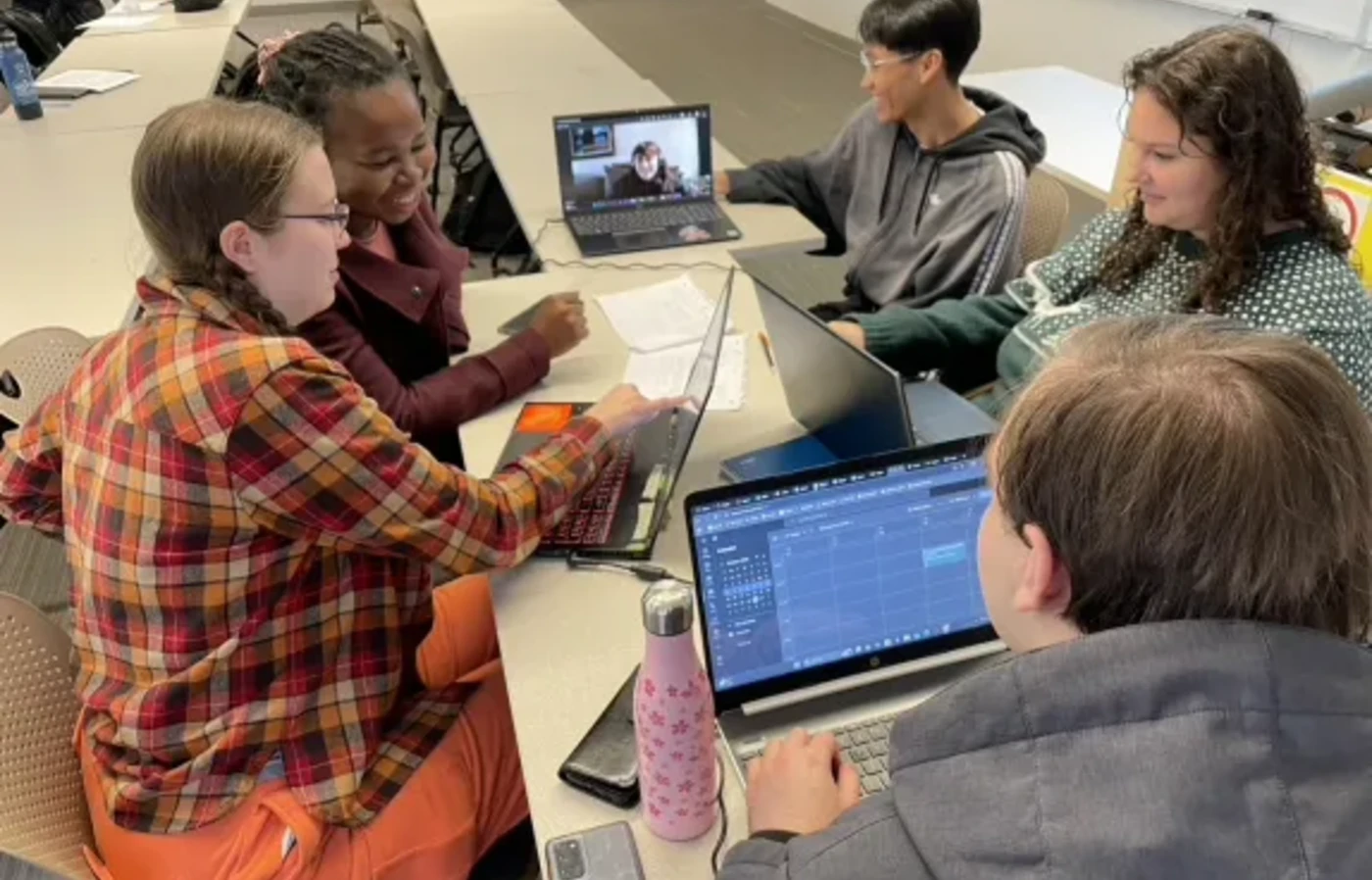 A group of business students sit around a narrow table with their laptops working together.