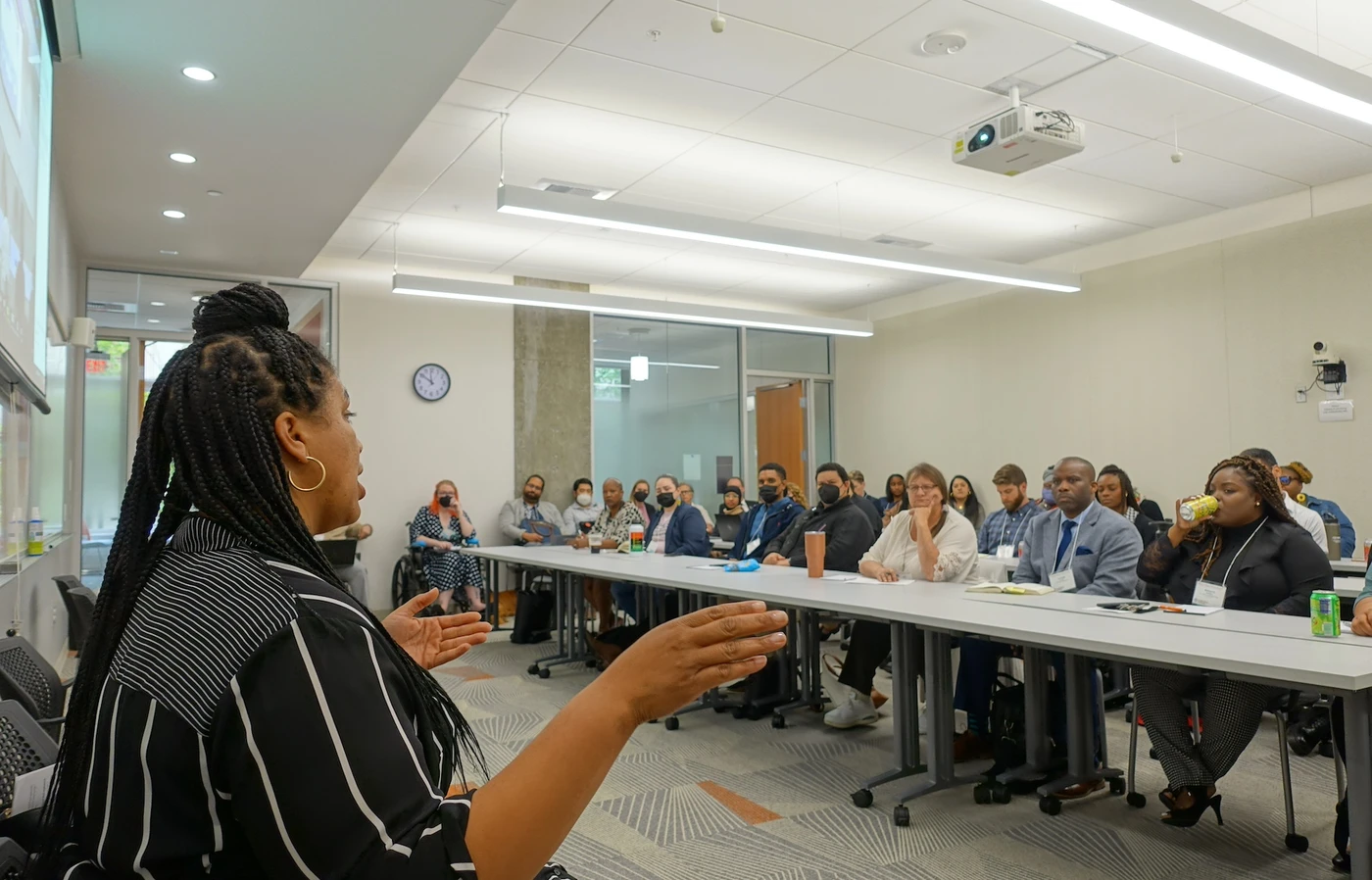 A Black woman in the foreground addresses a classroom of attendees.