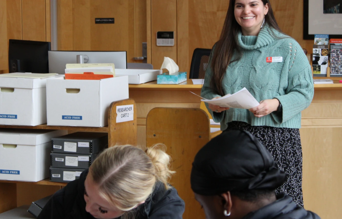 Archivist Natalia Fernandez looks on as students examine documents from archive boxes.
