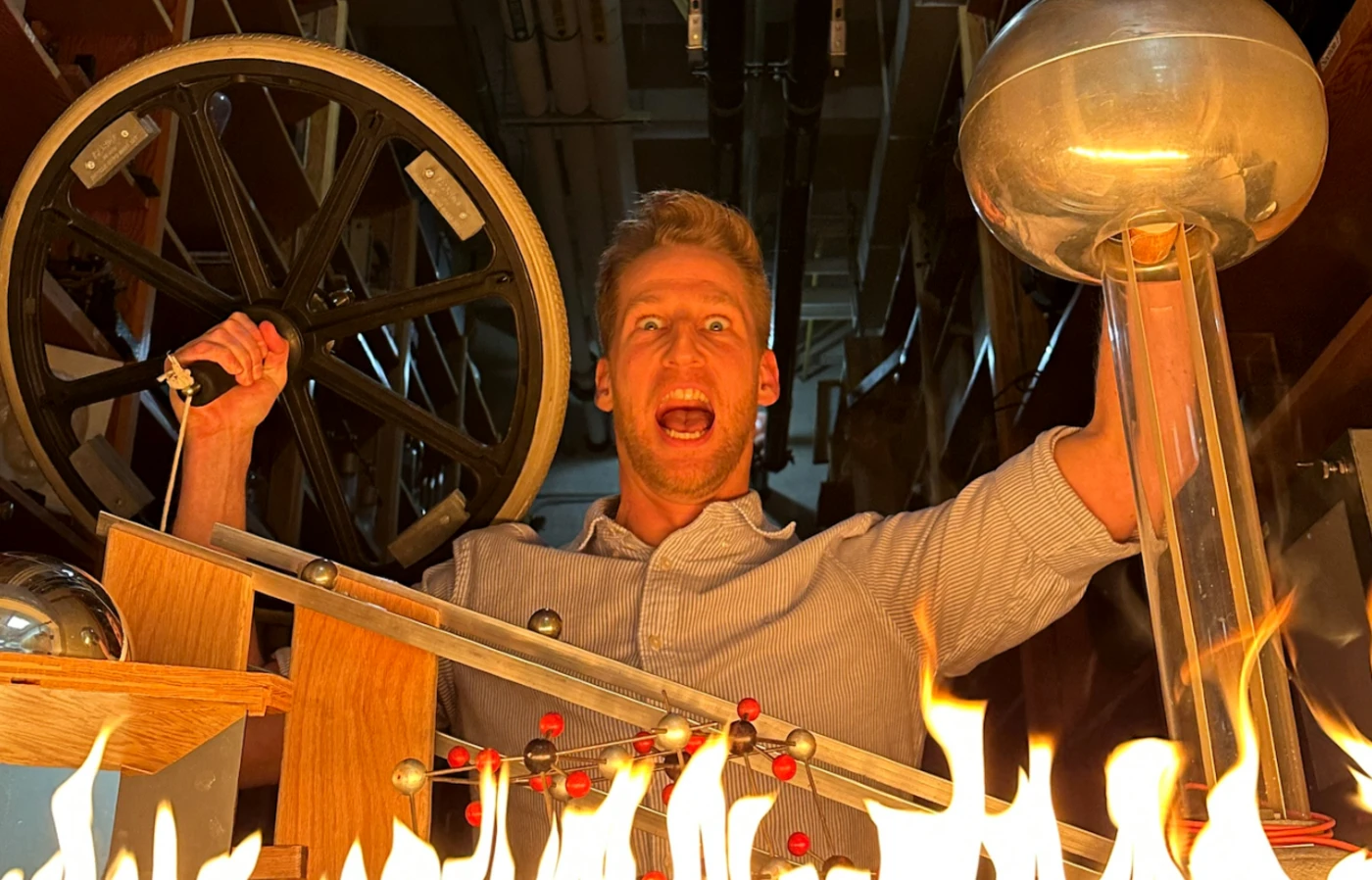 A mad scientist holds some physics instruments aloft behind a row of small flames, looking very dramatic.