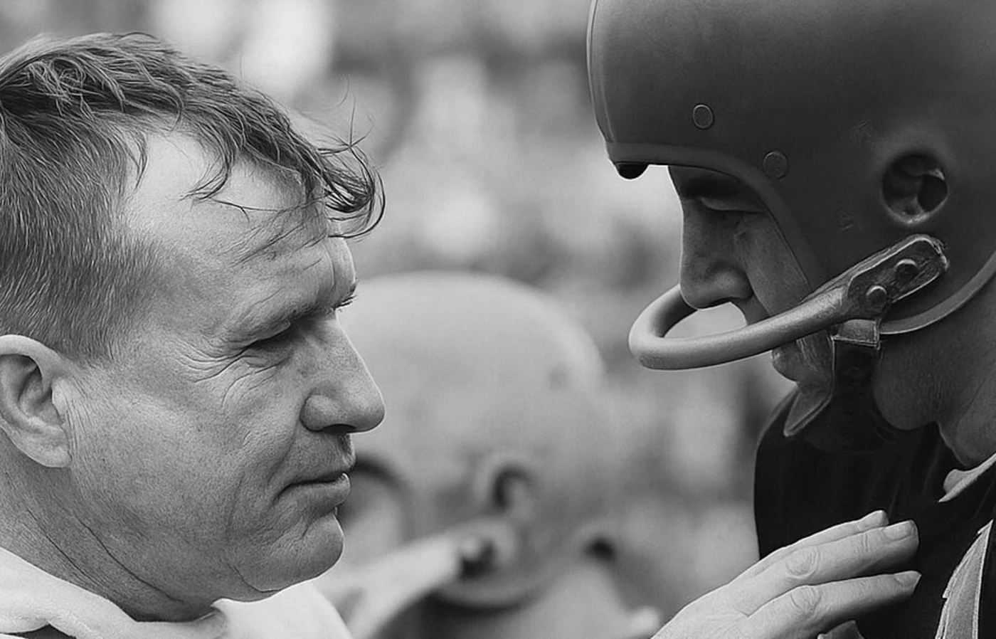 Black-and-white photo of a grizzled athletic trainer addressing a football player.