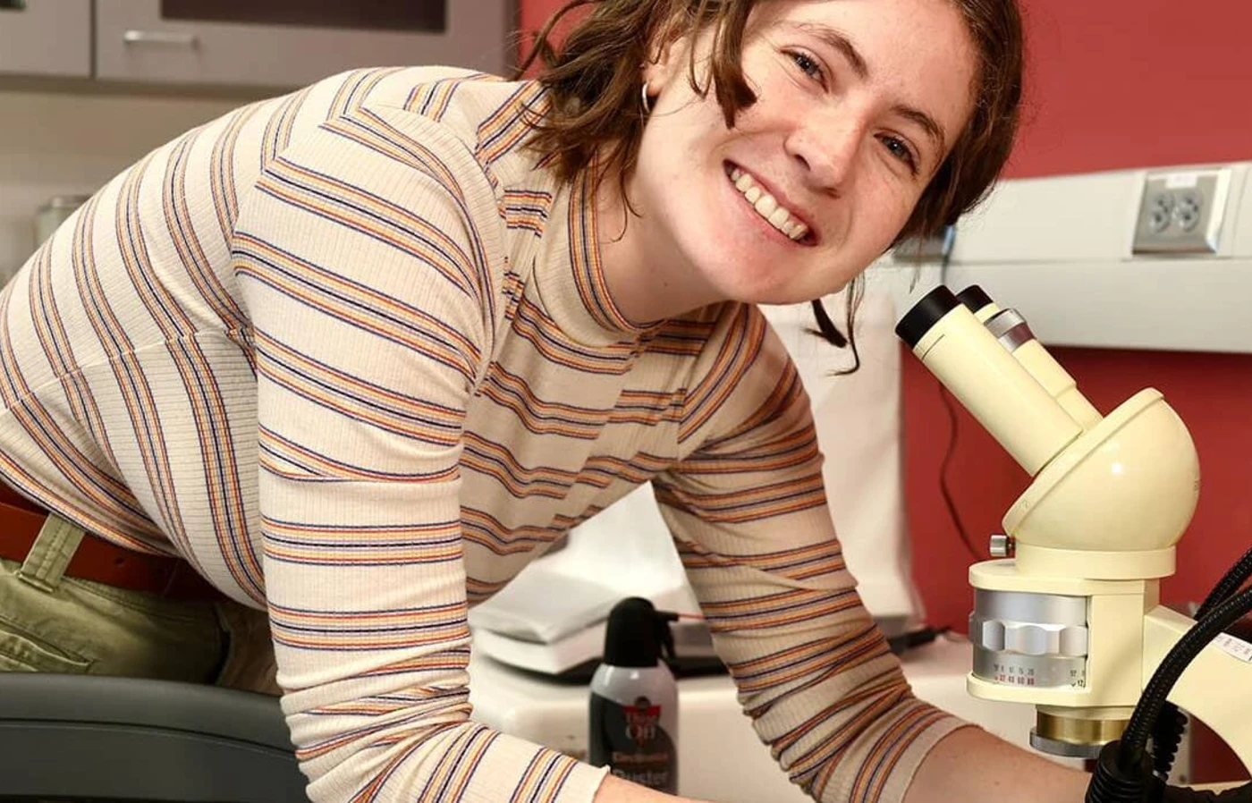 Cadence Russell leaning over a microscope and smiling for the camera.