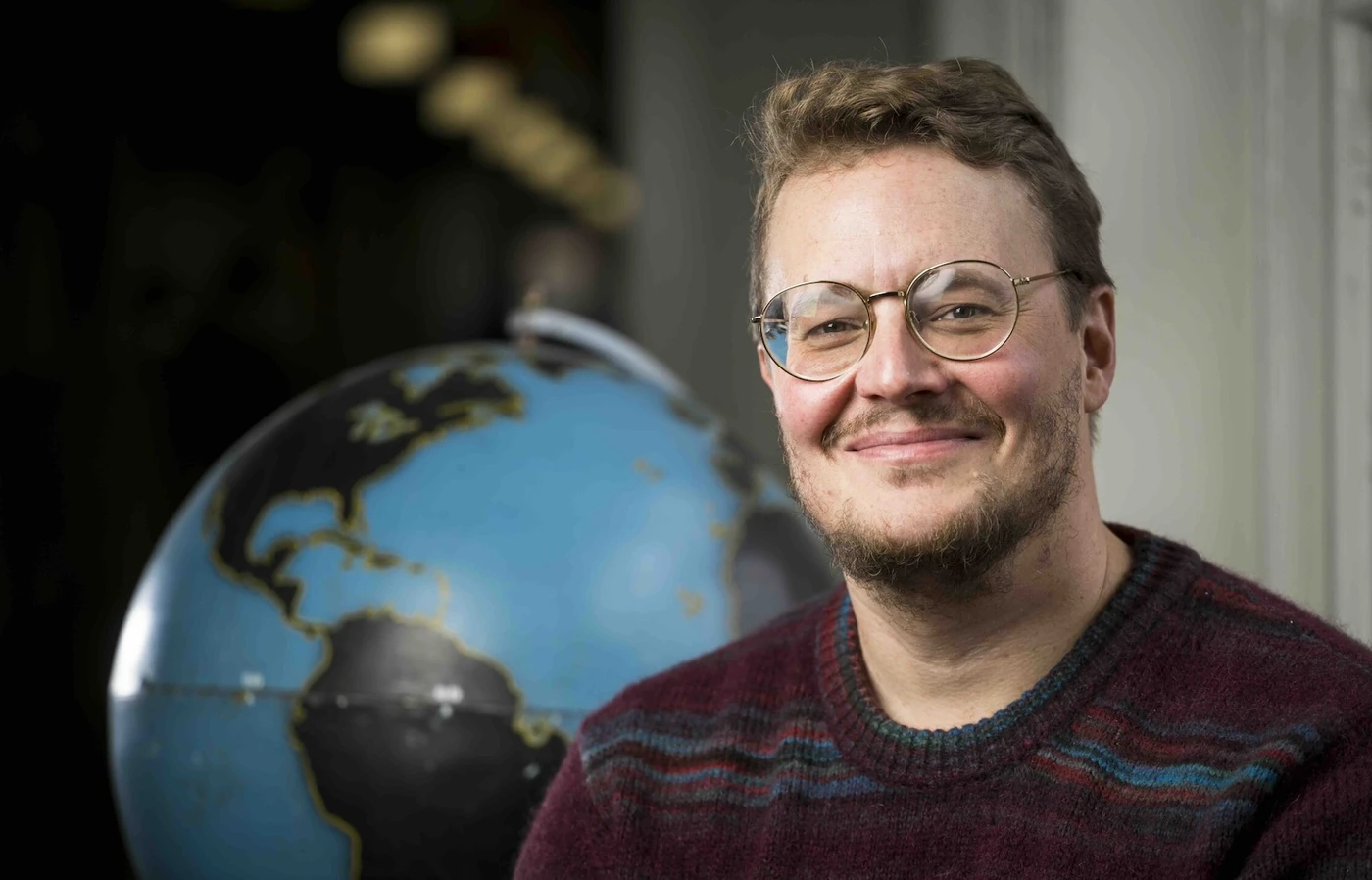Jamon Van Den Hoek sits in front of a globe.