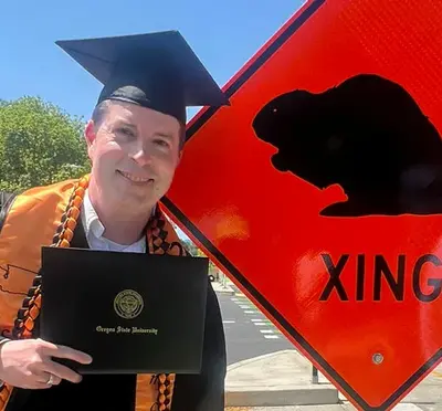 Graduate in front of beaver crossing sign