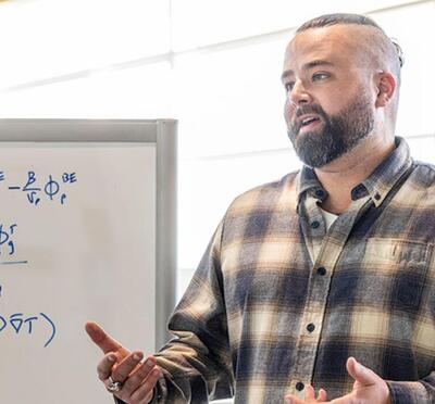Jackson Harter in a plaid shirt in front of a whiteboard covered in mathematical formulas.