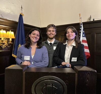 Three students smile at a podium flanked by the U.S. and Oregon state flags.
