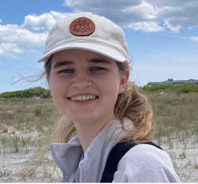 A young blonde woman in a baseball cap smiling on a sand dune.