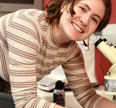 Cadence Russell leaning over a microscope and smiling for the camera.