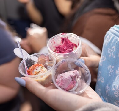 A hand with long painted fingernails clutches three small sample cups with colorful ice cream inside.