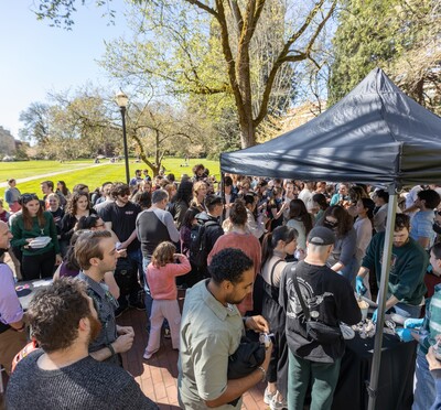 A throng of people around two canopies on the brick mall with the Memorial Union quad in the background.