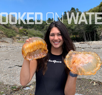 Olivia Boisen holding up two jellyfish on the beach.