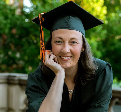 Christie Valencia sits with her chin in her hand, wearing her graduation cap and gown.