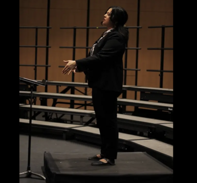Brenda Olvera in a black suit standing on a stage with empty risers.