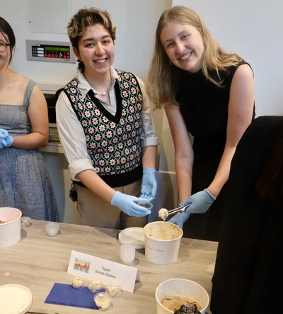 Two students on Team Scoop Sisters smile as they prepare to serve ice cream.