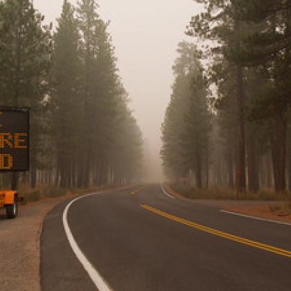 Image of sign indicating road closure due to forest fire with smoke heavy in the air.