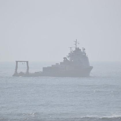 A vessel sits in the ocean, visible through hazy skies. 