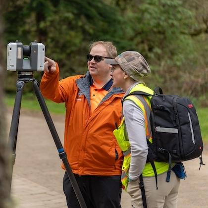 Image shows Prof. Mike Olsen with graduate student Dana Lind wearing a bright yellow safety vest as they look at a scanner perched on a tripod.