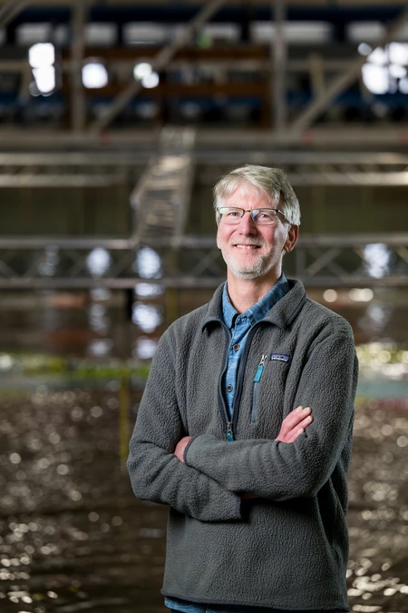 Dan Cox in a long-sleeved gray jacket standing in the wave lab. 