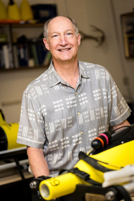 Jack Barth in a collared shirt standing behind a piece of bright yellow equipment.