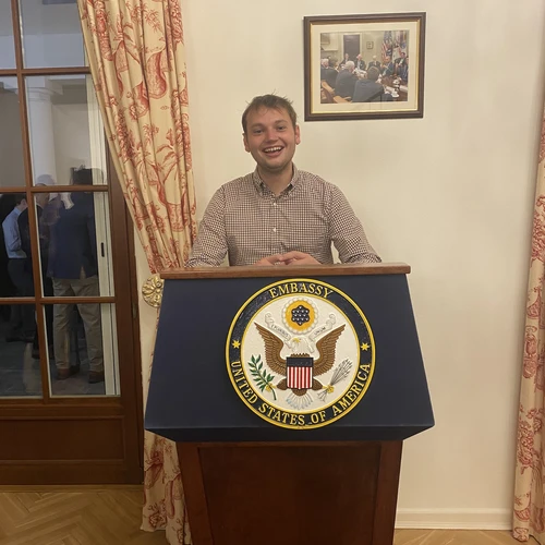 A young man standing behind a podium with a U.S. embassy seal on it.