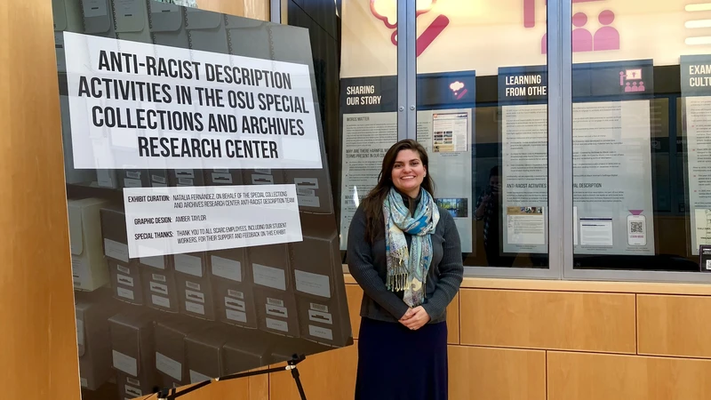 Archivist poses with exhibit panels detailing the archives' anti-racist description work.