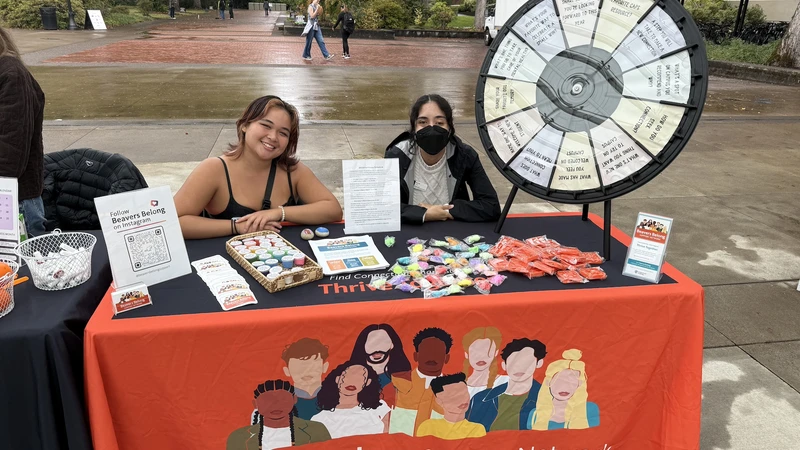 Two students sitting at a Beavers Belong Support Network table during an outdoor tabling event.