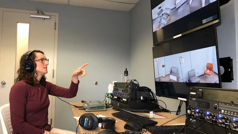 Clinic director Bridget Klest points at a pair of screens while wearing headphones.
