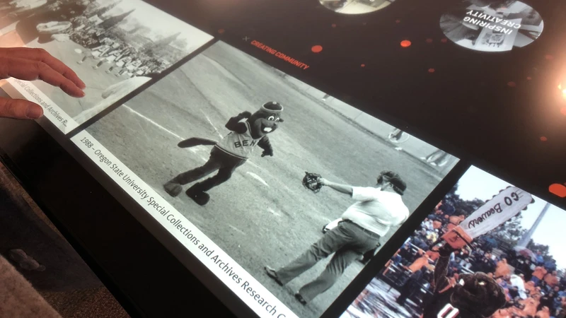 A story displayed on the OSU 150 touch table shows an old black-and-white photo of Benny the Beaver on a baseball field.