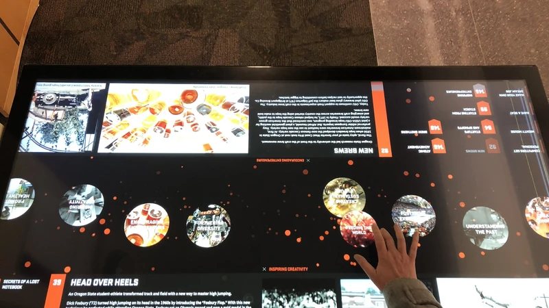 An overhead view shows a woman's hand navigating the interactive table's touchscreen.