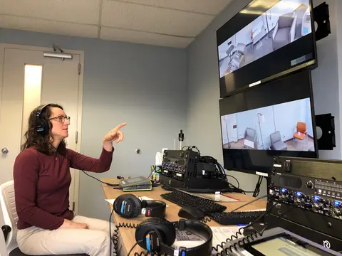 Clinic director Bridget Klest points at a pair of screens while wearing headphones.