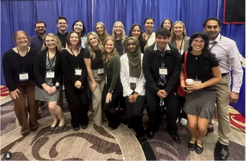 A group of undergraduate psychology students pose with Professor Regan Gurung at a conference.
