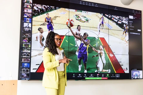 Former WNBA player Lisa Willis in a bright yellow suit in front of a screen displaying a basketball game.