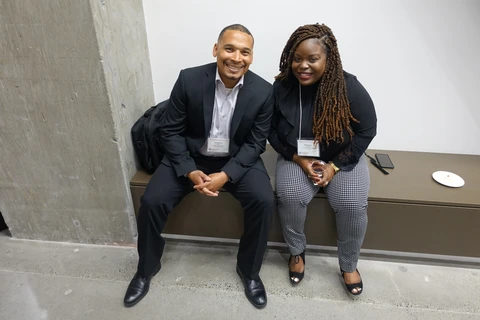 A Black man and woman sit side-by-side and smile for the camera.