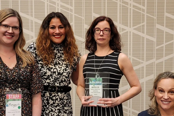 Disability psychology researcher poses with her award plaque alongside three other attendees.