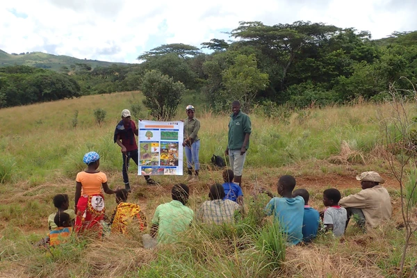 Mozambican master's students hold up a colorful poster outdoors as they teach kids about forest restoration.