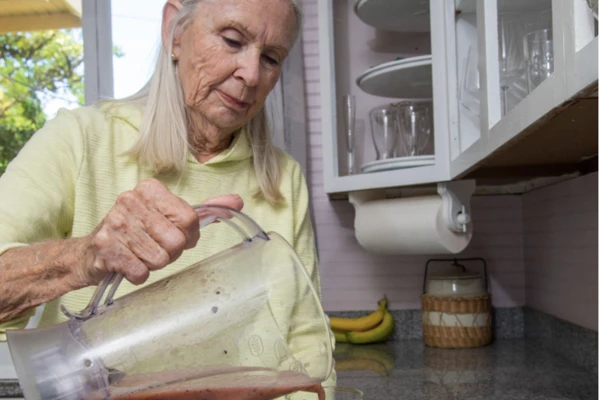 Woman with gray hair pours a smoothie.
