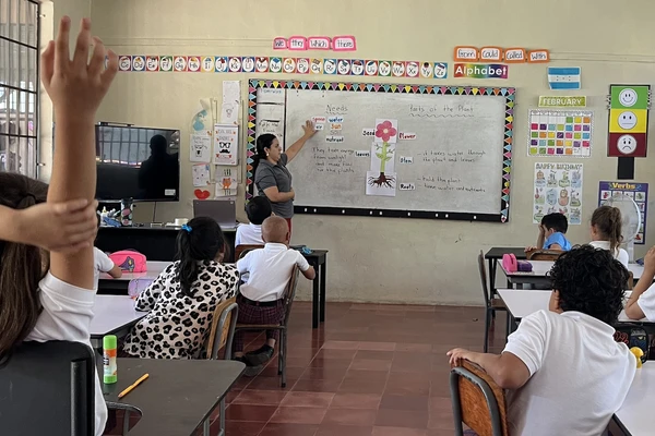 A classroom in Honduras with young students looking at their teacher writing on the white board.