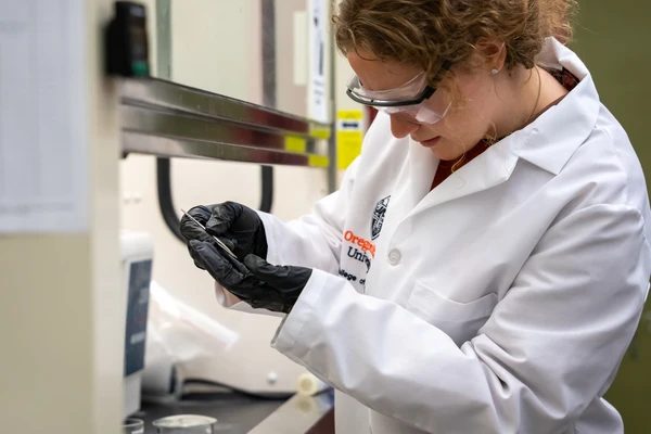 Madalyn Gragg in lab coat and safety glasses working at a lab bench.