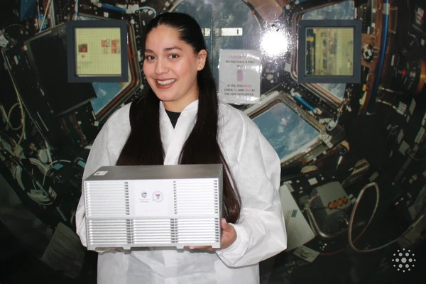 Ivana Hernandez wearing a white lab coat and holding a metal box of cell cultures to be sent to the International Space Station.