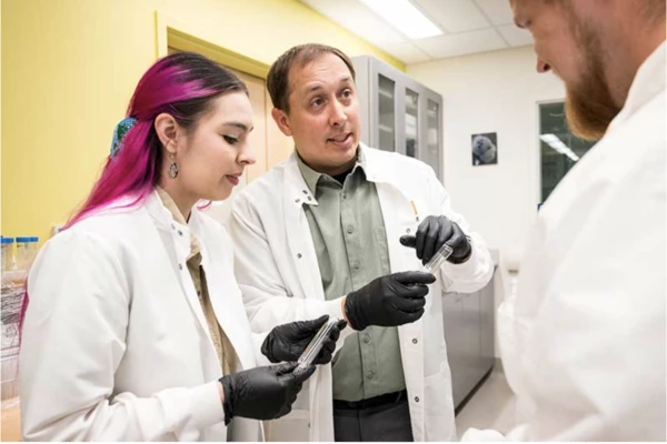 Brian Tattitch, center, with master’s student Sophia O’Barr and undergraduate Konstantin Lukyanenko, all in white lab coats in the lab.
