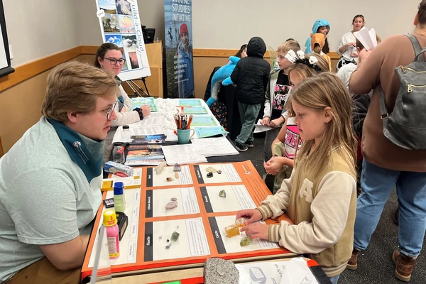 A grad student sits opposite a young girl while displaying chunks of minerals during Discovery Days.