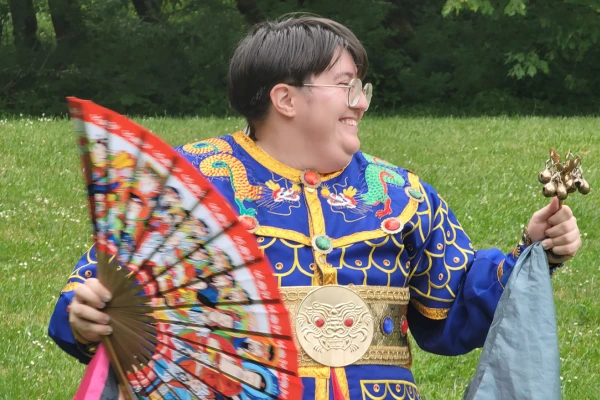 Counseling student Jay Gomez holds a large colorful fan and wears a blue traditional Korean outfit.