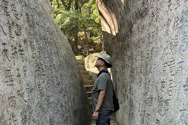 Professor Lei Xue stands in a narrow gap between two stone walls, reading inscriptions carved into the stone.