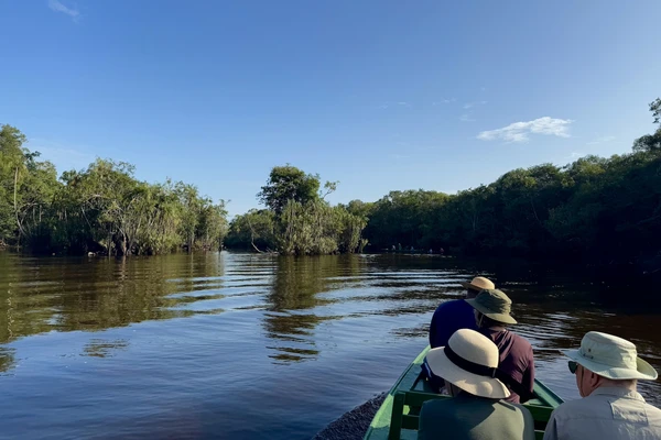 A small boat carrying a few researches glides along a small river in the Brazilian Amazon with rainforest on either side of the calm water.