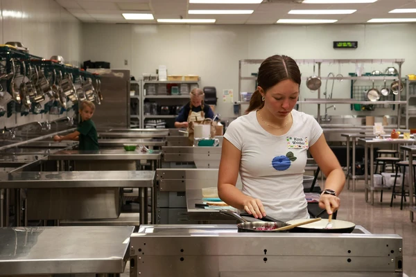 Kyah Weeber prepares food on a gleaming metal counter in an industrial-sized kitchen.
