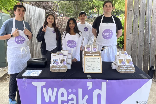 Students wearing white aprons pose behind a table selling their Tweak'd cupcakes.